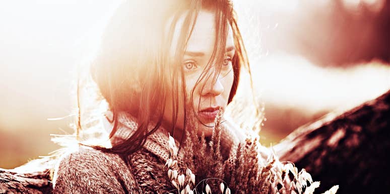Biochemical ways your brain tricks us into loving abusers woman looking sad holding flowers, sun behind her head