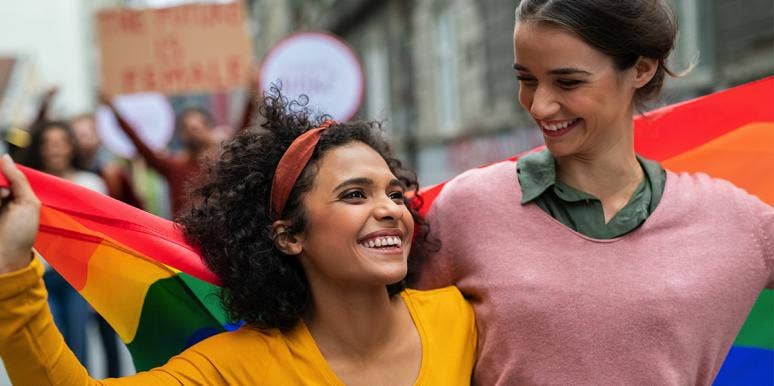 What The Colors In The Bisexual Pride Flag Mean & Why There Won't Be A Bisexual Flag Emoji couple draped in an lgbt flag