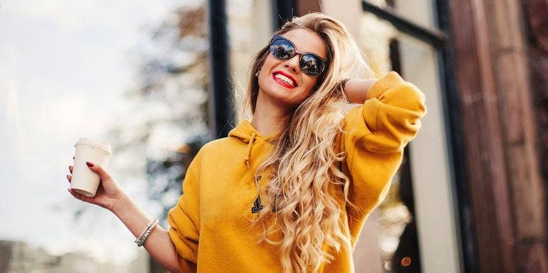 blonde woman smiling and wearing sunglasses while touching her hair