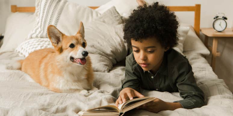 Boy reading a book on a bed with a dog