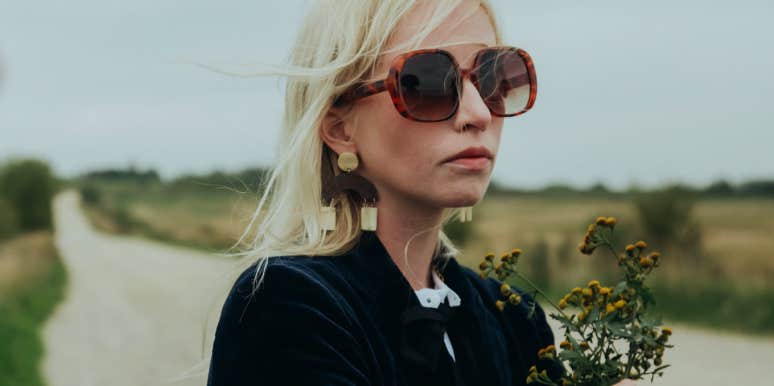 sad woman wearing sunglasses holding flowers
