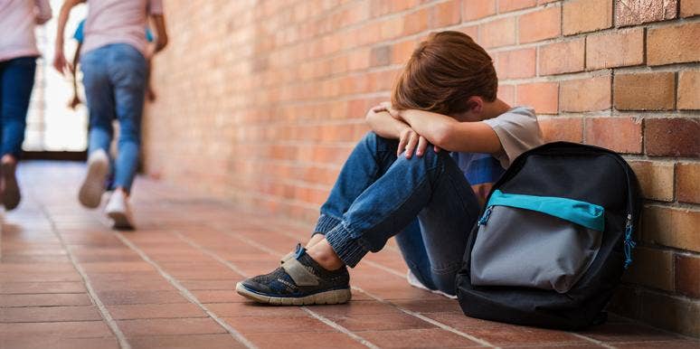 Things To Do Immediately If Your Child Is Being Bullied upset kid sitting against wall with his backpack