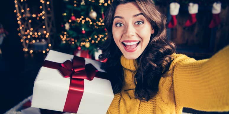 woman taking selfie for Instagram in front Christmas tree holding a present
