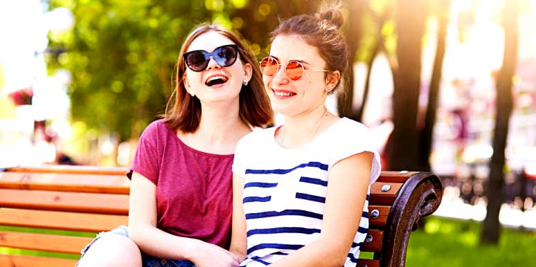 Two women sit on a park bench and laugh