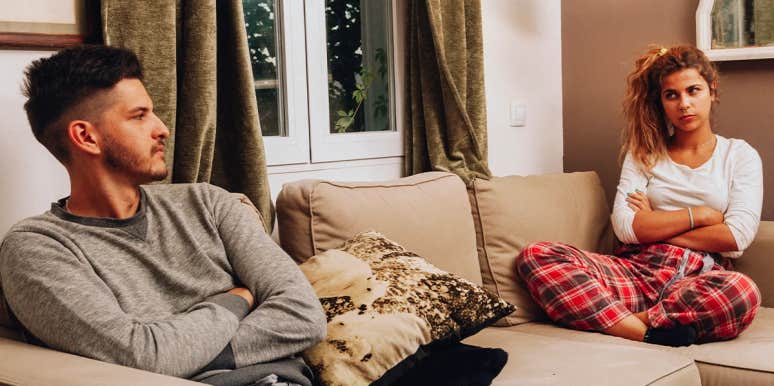 Why Contempt Is So Damaging In Relationships (And How To Prevent It In The First Place) couple looking angrily at each other with arms crossed on couch