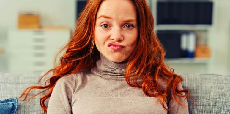 Pretty young redhead woman pulling a funny face making an exaggerated grimace with her lips as she sits on a sofa at home
