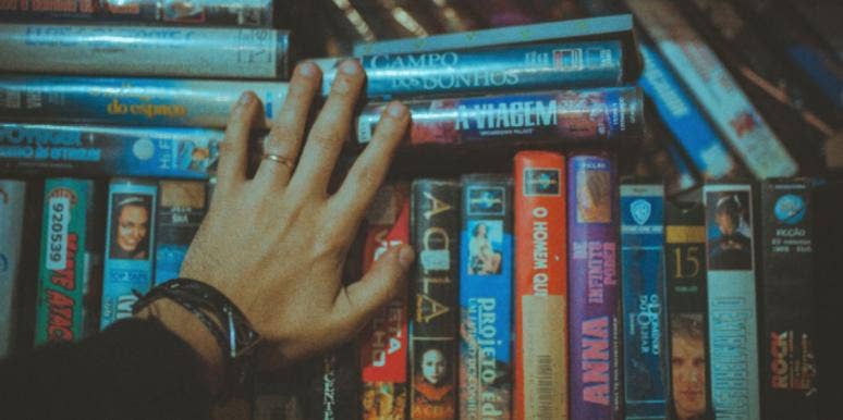 31 Best End Of The World Movies - Apocalyptic Movies To Watch person's hand on a stack of movies