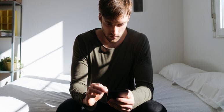 If A Guy Behaves This Way On Facebook, Sorry ... He's Not Into You man looking at phone while sitting on bed