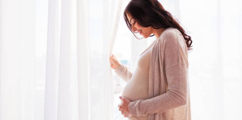 pregnant woman smiling holding belly in front of window