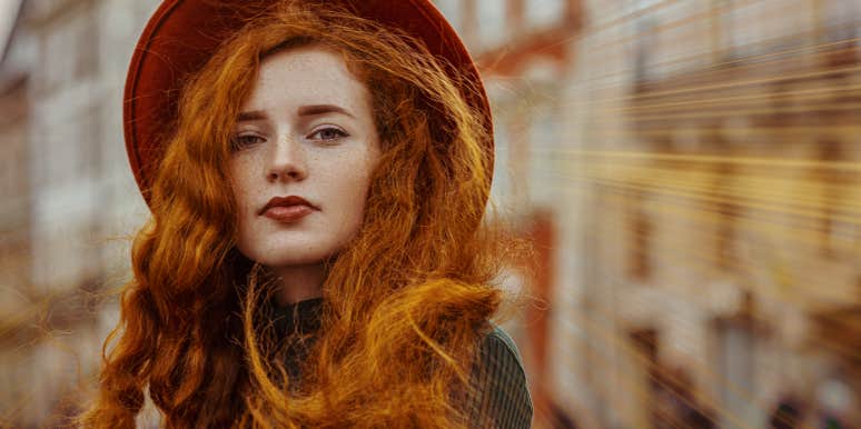 redhead woman with long hair looks at camera, wearing dark red hat