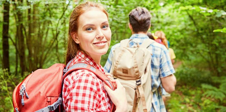 Smiling woman dressed in red hiking through green woods.