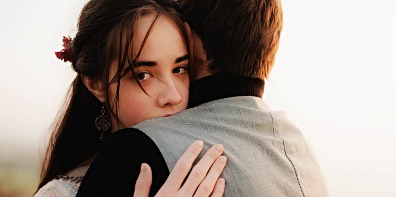 woman looks into camera with sad eyes, hugging a man