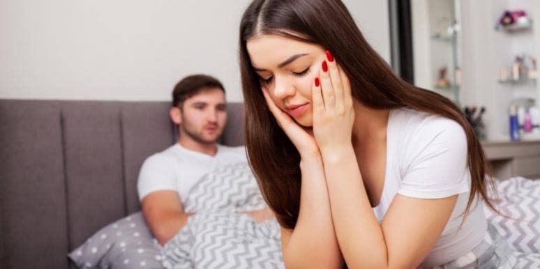 The Harsh Reality Of Being The One Who Loves Less woman with head on hands man in bed behind her
