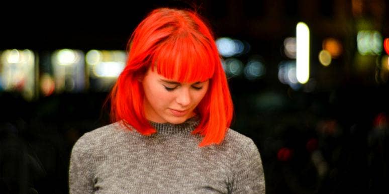 Is Shingles Contagious? How I Got Shingles More Than Once young white woman with bright red dyed hair in a beige sweater looks down, seemingly in pain