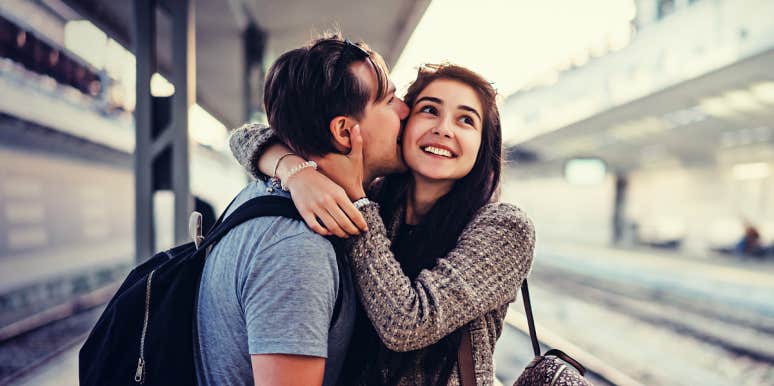 man kissing a woman on a train platform while she laughs 