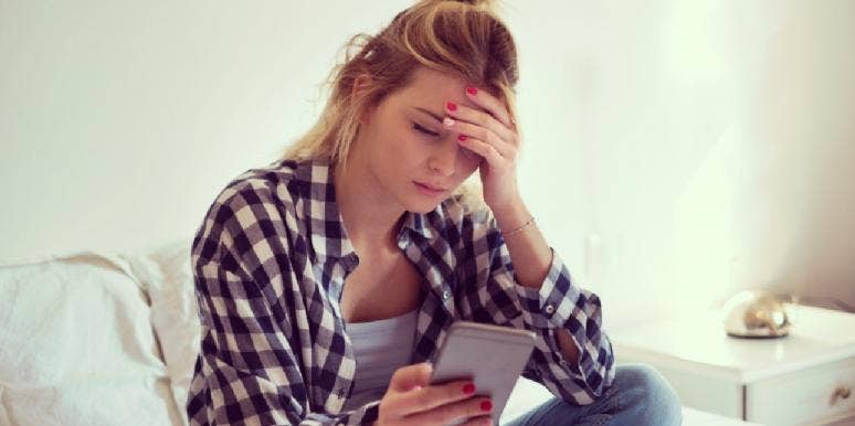 upset woman looking at her phone hand on her face