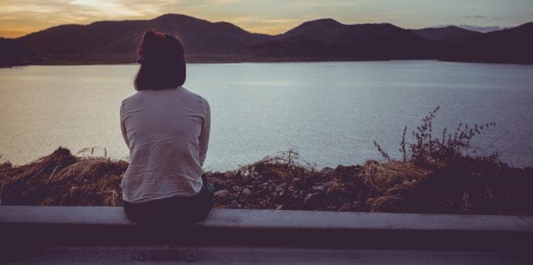 How To Fall Out Of Love With Someone — 7 Tips To Help You Let Go woman sitting looking out at a pretty landscape