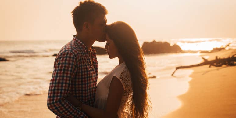 man kissing woman's forehead on beach