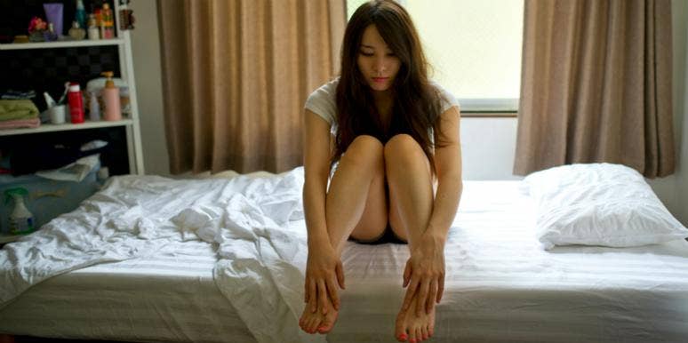 brunette woman sits on the edge of a bed looking sad