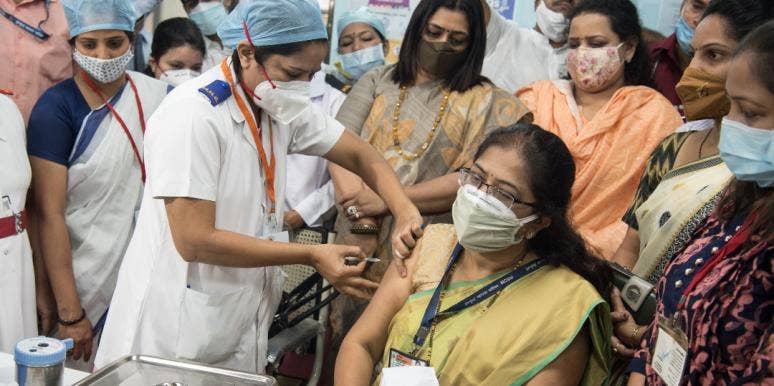 Covid In India, And One Family's Story Of Perseverance woman getting a vaccine in india while a crowd watches