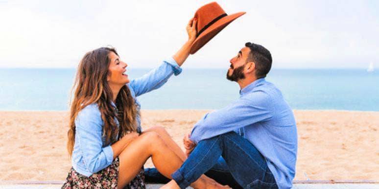 guy and girl smiling on the beach with a hat