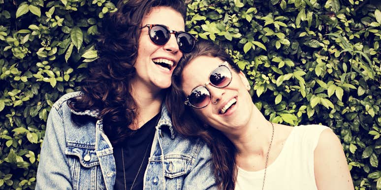 two brunette women in glasses laughing, one's head on the other shoulder