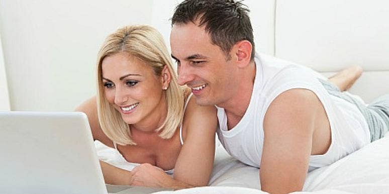 man and woman looking at laptop in bed