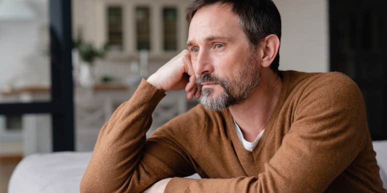 depressed man with hand on head looking out window