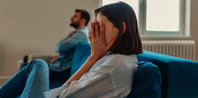 woman putting hand over eyes next to man on couch