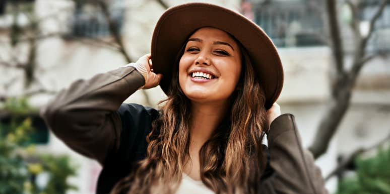 smiling brunette outside in a brimmed hat and jacket