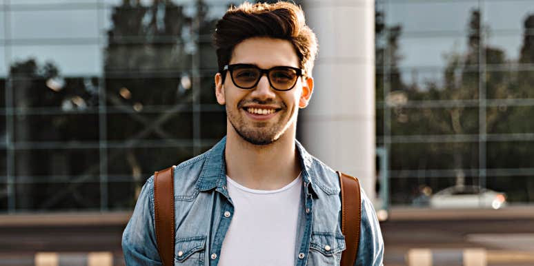 young man with dark hair and glasses smiles at camera