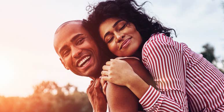price of emotional labor on women in relationships couple cuddles with the sunset behind them near a lake