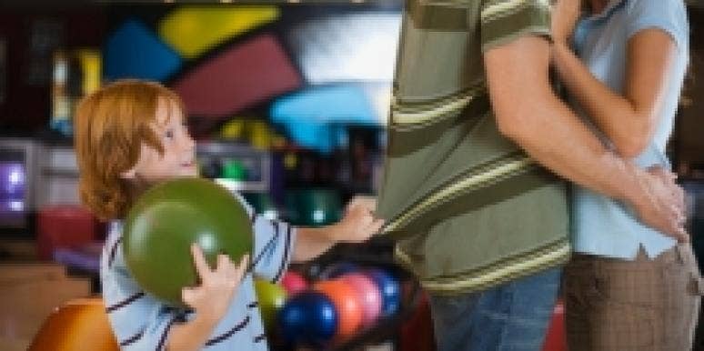 mom and dad kissing with child watching at bowling alley