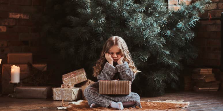 Mom Refuses To Make Christmas Plans With $100 Budget Sad kid sitting in front of an undecorated Christmas tree.
