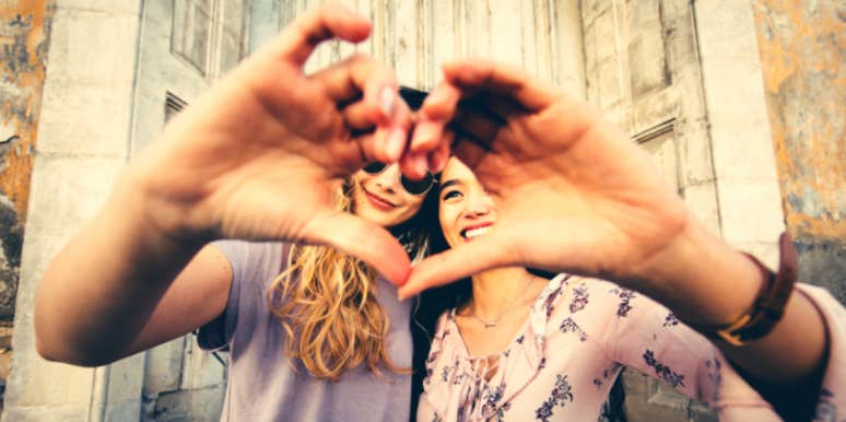 two women holding their hands up in a heart shape