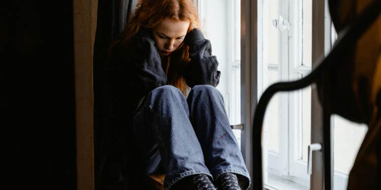 sad woman sitting at windowsill