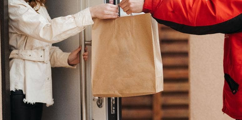 A food delivery driver is handing food to a woman.