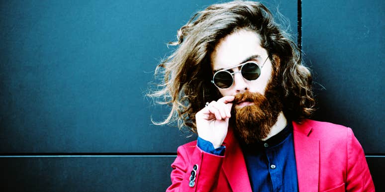 5 Reasons It's Hard To Love A Man With Mommy Issues man with long hair wearing bright pink suit plays with his hipster mustache