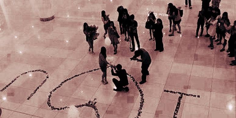 7 Reasons Not To Propose To The One You Love At A Family New Year's Eve Party A man gets down on one knee surrounded by rose petals spelling out "I heart you" to propose to his girlfriend that he loves and give her an engagement ring at a New Year's Eve party in front of her family and friends.