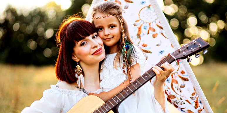 hippie mom with guitar, snuggling young daughter in a field