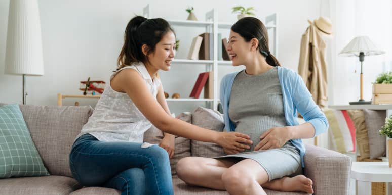 woman touching pregnant woman's stomach while sitting on couch