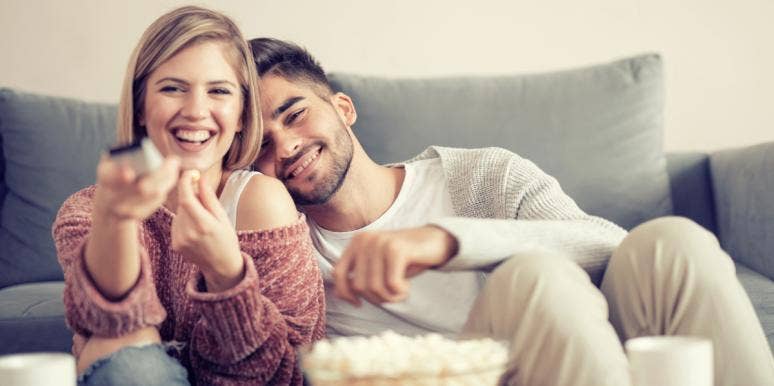 man and woman cuddling on couch with TV remote and popcorn
