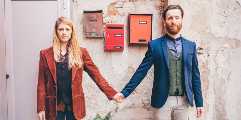 quirky couple stands in front of a series of red mailboxes, holding hands