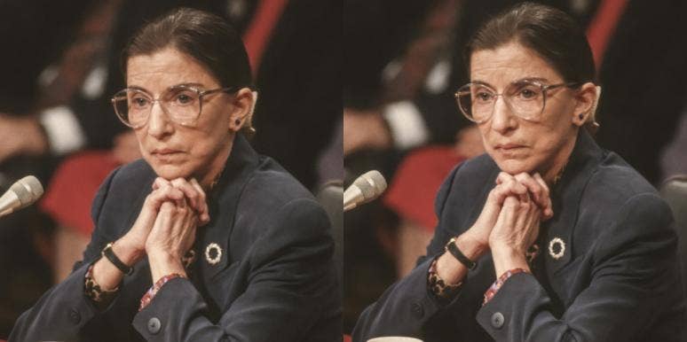 Justice Ruth Bader Ginsburg, in middle age, sits in front of a microphone wearing a grey suit, listening intently