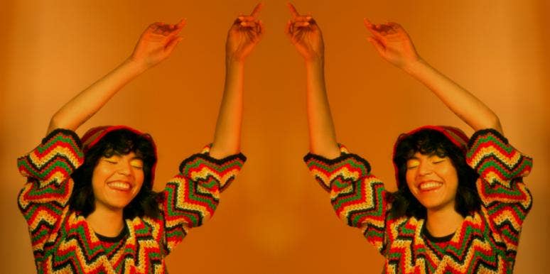 14 Pros And Cons Of Loving A Scorpio (Buckle Up For A Wild Ride!) woman with her arms up in the air on orange background