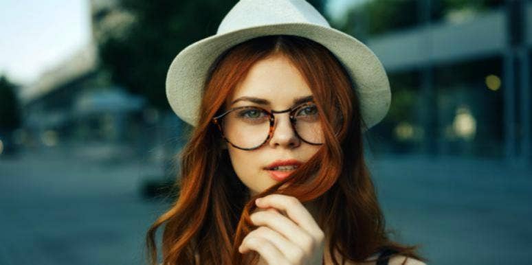 Self Sabotage: Why You Do It & How To Stop Self-Sabotaging young brunette in tortoise-shell round glasses and a white hat looks into camera and coyly plays with hair