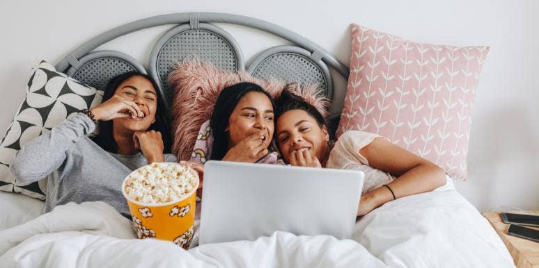 50 Fun Sleepover Ideas You’ll Enjoy No Matter Your Age 3 girls watching movies on a laptop eating popcorn
