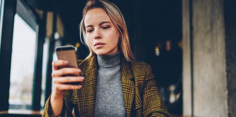 Your Social Media Activity Could Be Used To Diagnose A Psychiatric Disorder young woman looks at her phone, wearing aa jacket in a cafe