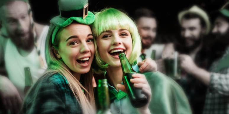 two young white women in St. Patrick's Day garb, hold beers in a bar