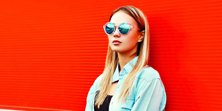 blonde woman in sunglasses looking angry against red wall
